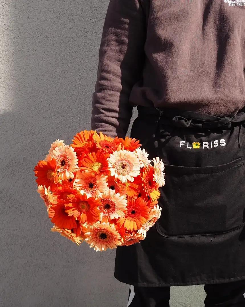 Ansatt i Floriss-forkle holder en bukett med oransje germini i butikken på Østfoldhallen